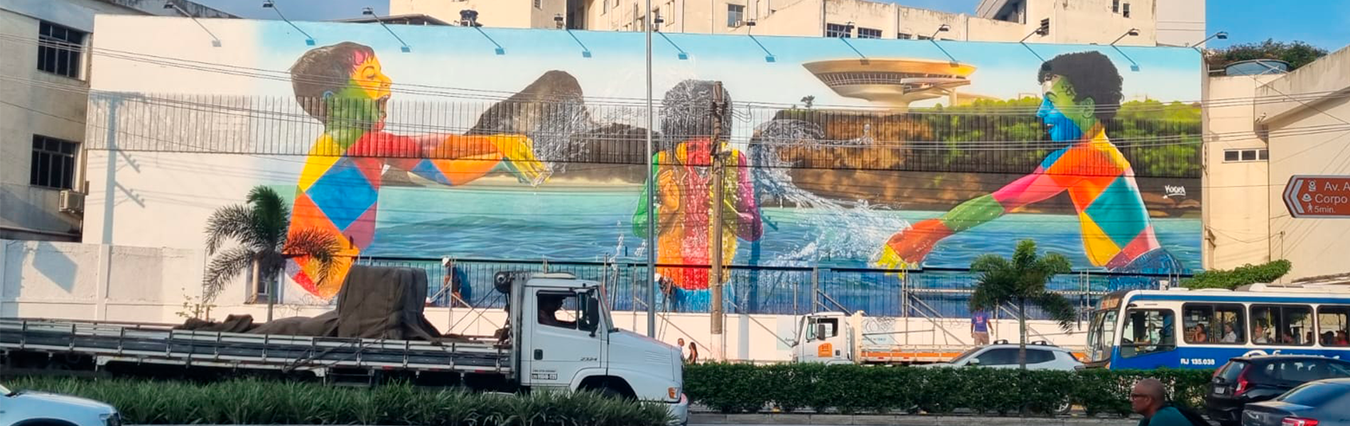 Muro pintado mostrando três crianças coloridas brincando na água. Ao fundo o museu de arte contemporânea de Niterói.