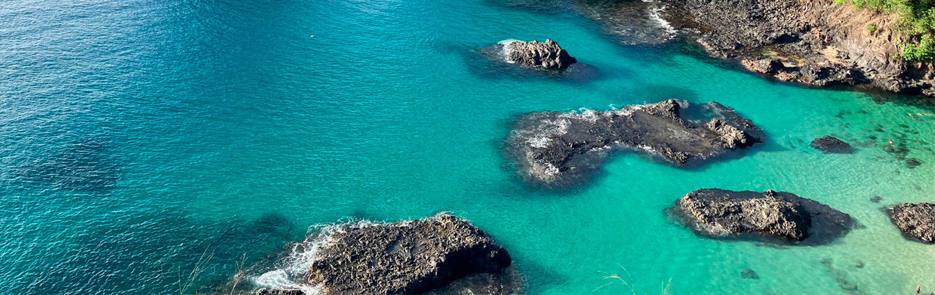 Foto de mar azul e duas grandes pedras perto da costa de uma praia.