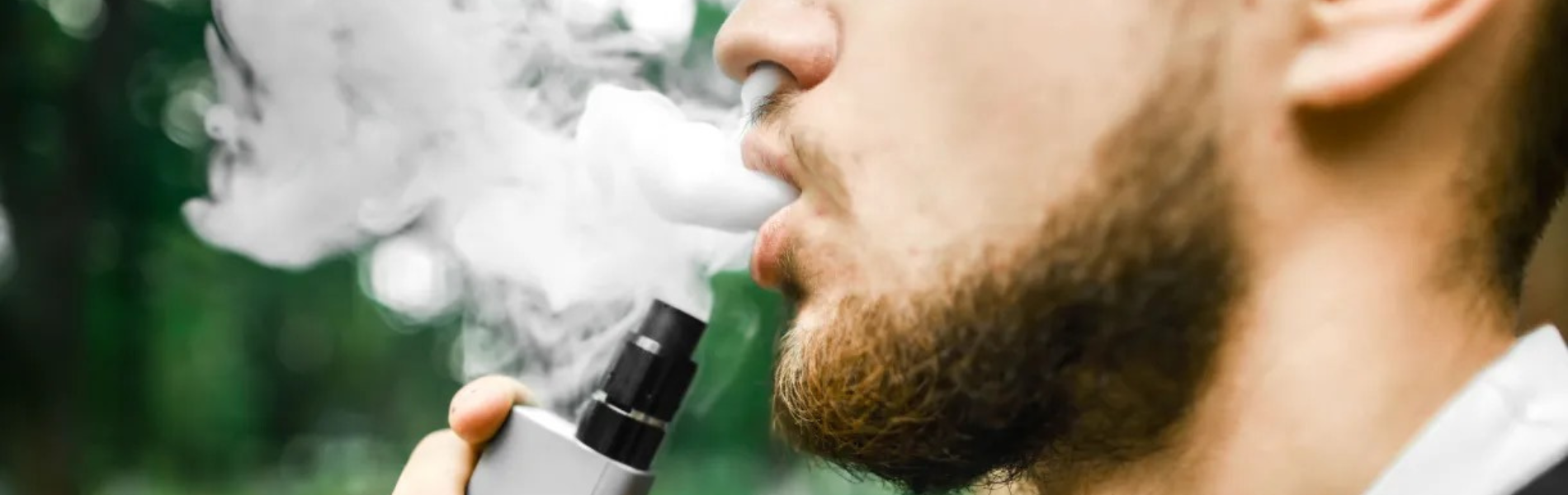 Foto de homem segurando um cigarro eletrônico e soltando fumaça pela boca e nariz