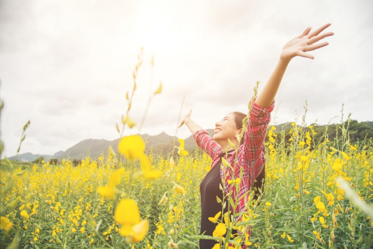 Imagem: mulher em um campo florido de braços abertos