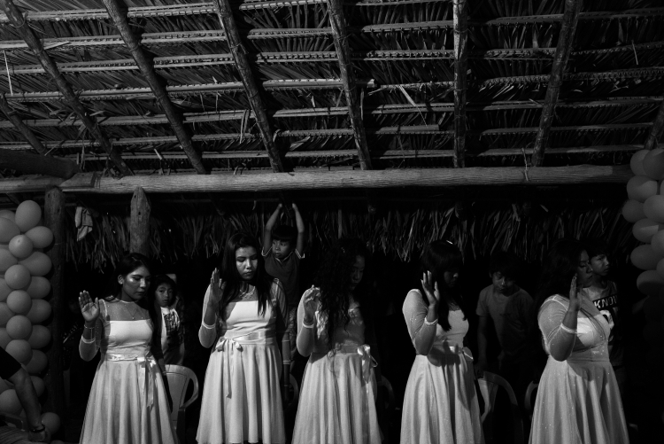 imagem de mulheres indígenas, vestidas de branco, dentro de uma oca, participando de uma festividade religiosa