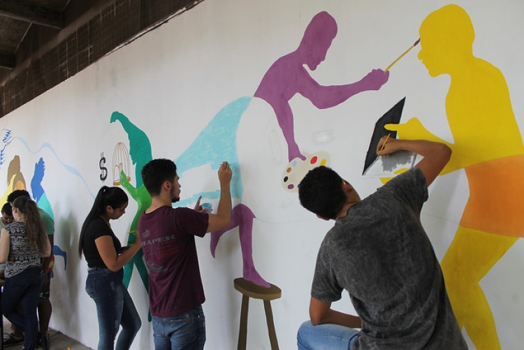 Imagem: alunos pintando silhuetas coloridas em um muro branco