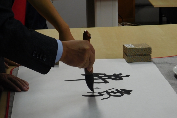 Mão pintando caracteres chineses em uma folha de papel branca.