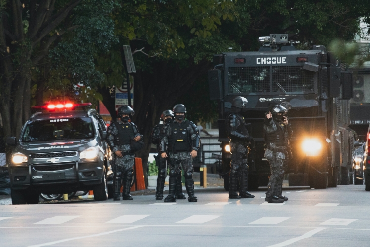 Carro da polícia de choque, policiais e camburão de choque parados em uma avenida