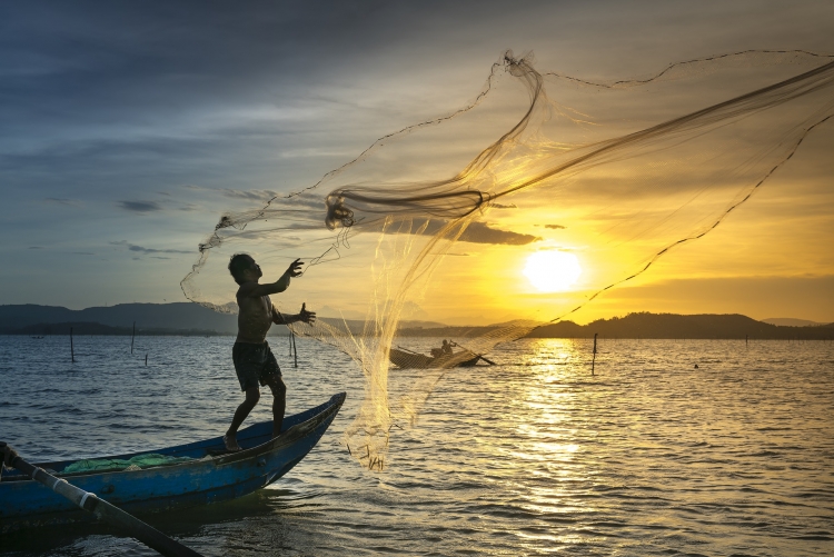 pescador em um barco no mar jogando uma rede de pesca na água
