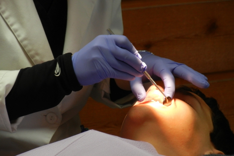Mãos de dentista com luva azul manipulando a boca de um paciente com um instrumento 