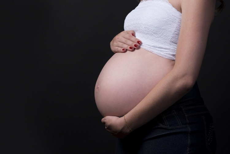 Mulher grávida de perfil com a barriga de fora, sobre um fundo preto