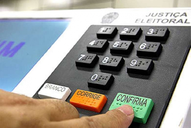 Pessoa tocando no botão confirma da urna eletrônica durante processo eleitoral