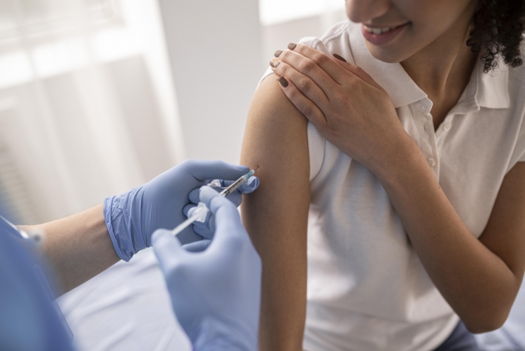 imagem de fundo branco, mulher segurando a manga da camisa enquanto outra pessoa aplica a injeção em seu braço