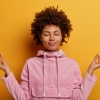 Imagem fundo laranja, menina negra de roupa rosa fazendo pose de meditação