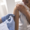 imagem de fundo branco, mulher segurando a manga da camisa enquanto outra pessoa aplica a injeção em seu braço