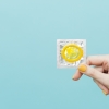 Imagem fundo azul, mão segurando um preservativo amarelo