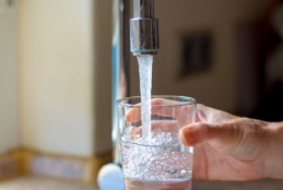 Mão segurando um copo de água que está abaixo de uma torneira aberta