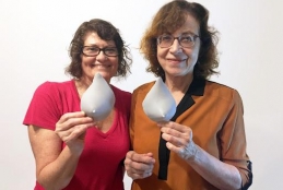 Duas mulheres lado a lado segurando, cada uma, um protótipo em 3D de seio