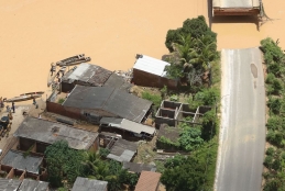 Imagem aérea que contém telhados, uma rodovia partida ao meio e água barrenta chegando aos telhados das casas