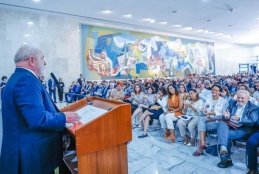 Foto do encontro de reitores e diretores das Instituições Públicas de ensino superior. Na imagem, o presidente Lula está com um terno de cor azul, em pé em um púlpito realizando o discurso. Na sua frente, a plateia está sentada e é composta por representantes de Universidades e Institutos Federais