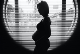 Silhueta de uma mulher grávida, de perfil, de frente para uma janela. Foto em preto e branco.