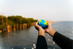 imagem com duas mãos segurando um globo terrestre e no fundo um rio