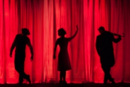 Cortina vermelha de teatro com silhueta de três pessoas refletida