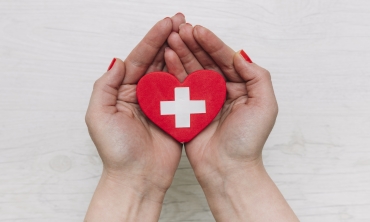imagem: par de mãos segurando um coração vermelho com o desenho de uma cruz branca