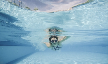 Imagem: mulher com óculos de mergulho nadando em uma piscina azul
