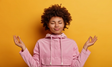 Imagem fundo laranja, menina negra de roupa rosa fazendo pose de meditação
