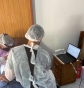 Dois profissionais da odontologia com touca e capa protetora, de costas, manipulando um paciente enquanto observam à direita a tela de um laptop
