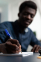 Rapaz negro de camisa azul, escrevendo em um caderno com uma caneta azul