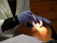 Mãos de dentista com luva azul manipulando a boca de um paciente com um instrumento 
