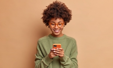 Mulher negra sorrindo e observando tela de celular 
