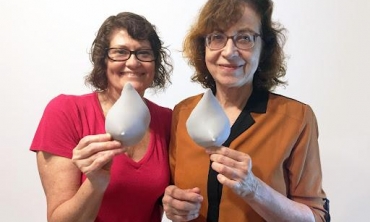 Duas mulheres lado a lado segurando, cada uma, um protótipo em 3D de seio