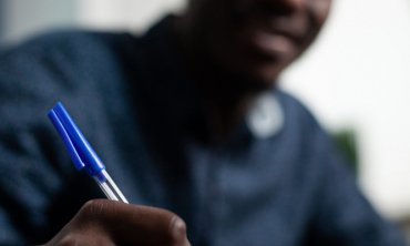 Rapaz negro de camisa azul, escrevendo em um caderno com uma caneta azul