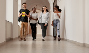 grupo de quatro estudantes multirraciais caminhando pelo corredor de uma faculdade