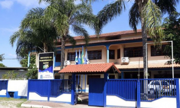 imagem de um prédio de dois andares de portão azul, árvores em seu terreno e algumas bandeiras