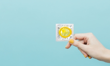 Imagem fundo azul, mão segurando um preservativo amarelo