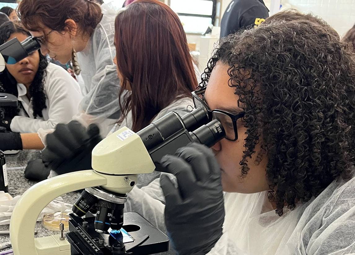 menina de cabelos cacheados olhando por um microscópio