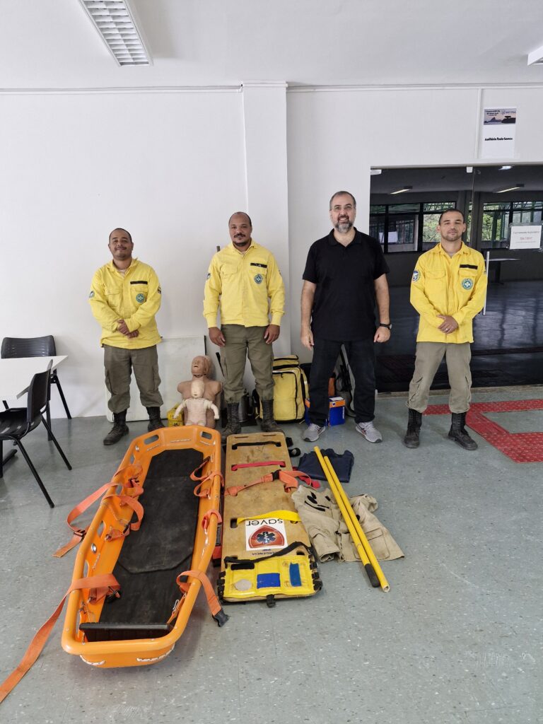 Integrantes da equipe de guarda-parques e participantes do treinamento posam no Instituto de Física da UFF ao lado de equipamentos utilizados em ações de resgate e combate a incêndios florestais, como maca de salvamento, prancha de imobilização e materiais de primeiros socorros.