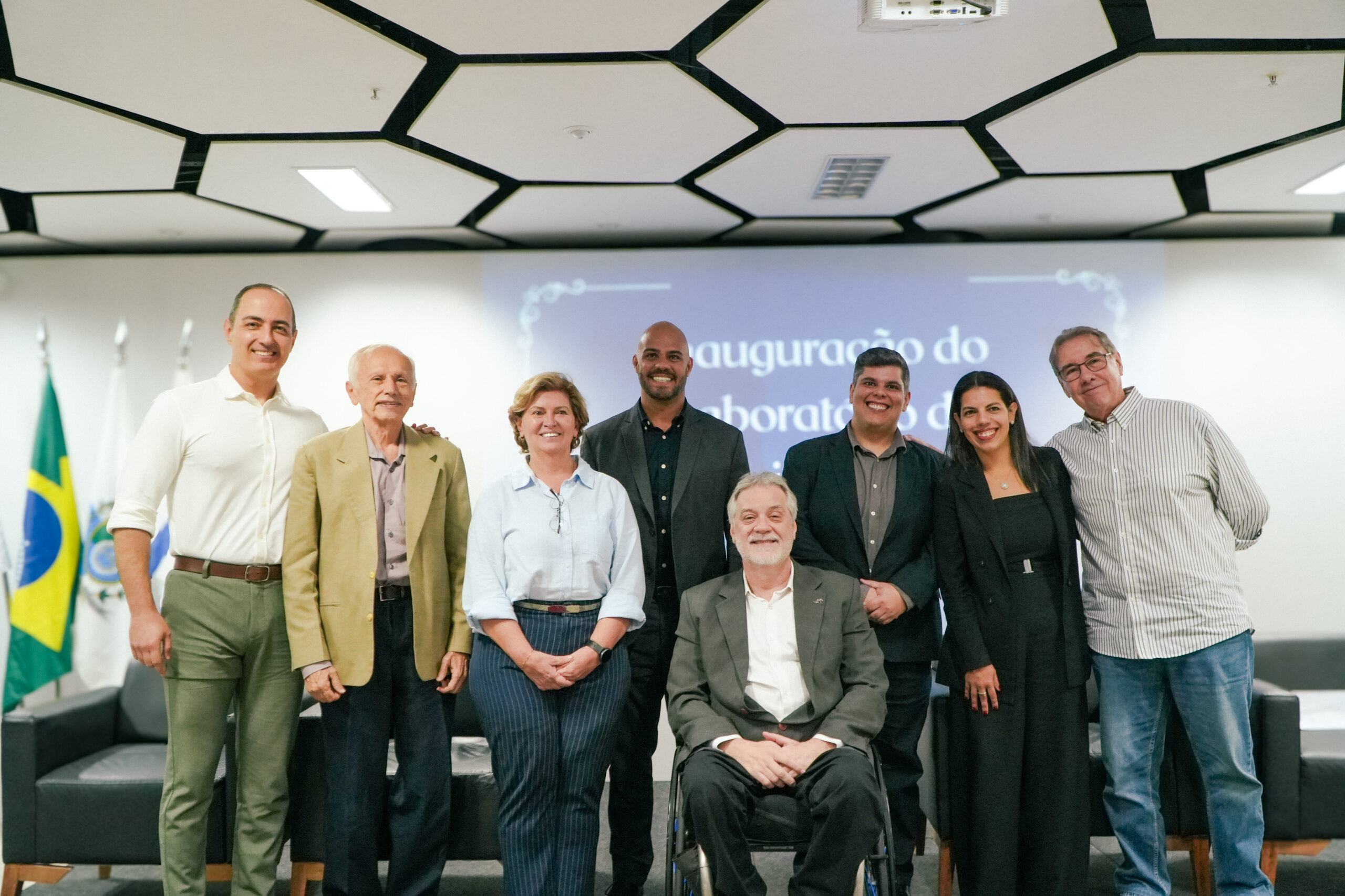Grupo de oito pessoas posa sorrindo para foto em evento de inauguração, com bandeiras ao fundo.