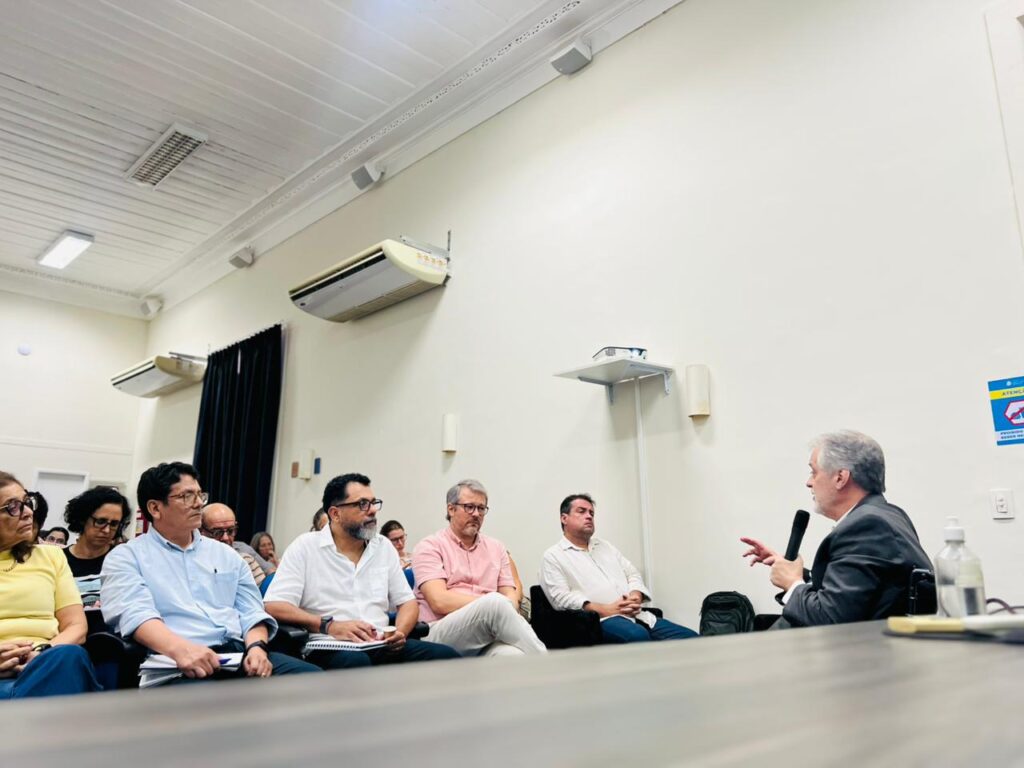 Imagtem de uma sala cheia. Um homem falando e o grupo ouvindo atentamente.