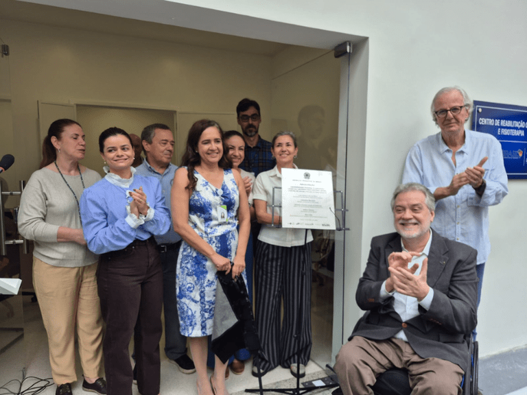 Foto: Comunicação HU Grupo de pessoas reunidas em frente à placa de inauguração de um centro de reabilitação e fisioterapia, enquanto alguns participantes aplaudem durante a cerimônia.